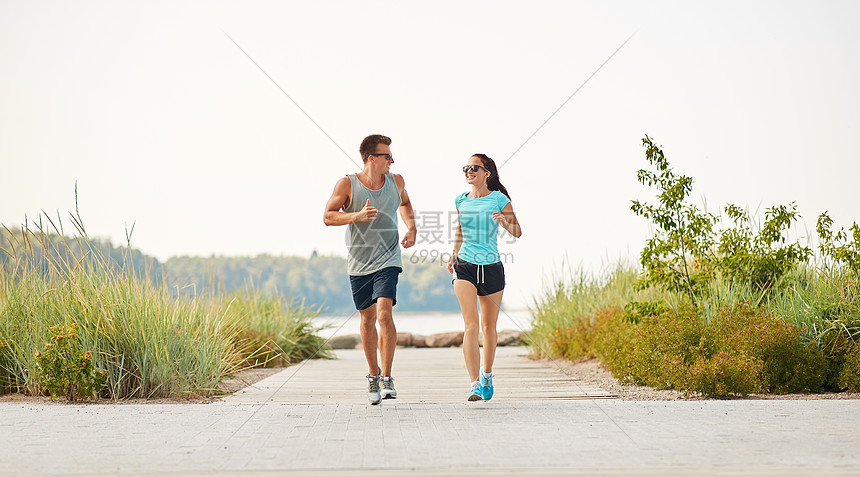 ‘~健身,运动生活方式的快乐的夫妇穿着运动服太阳镜沿着夏天的海滩小径跑步穿着运动服的夫妇沿着海滩小路跑步  ~’ 的图片