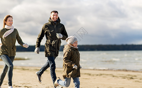 家庭,休闲人的快乐的母亲,父亲小女儿沿着秋天的海滩跑步幸福的家庭沿着秋天的海滩奔跑图片