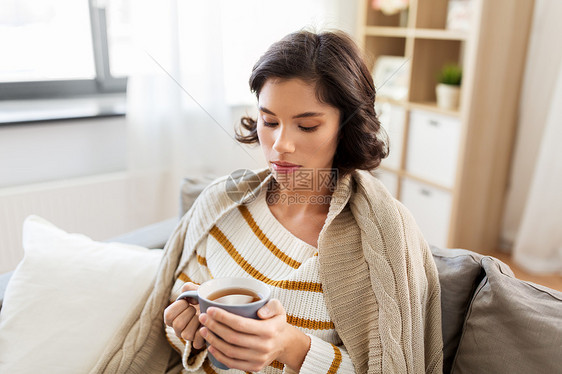 健康,寒冷人的悲伤的生病的轻女人坐沙发上,家喝热茶悲伤的生病的轻女人家喝热茶图片