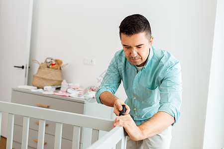 父母,父亲托儿所的快乐的中父亲与螺丝刀装婴儿床家里快乐的父亲用螺丝刀装婴儿床图片
