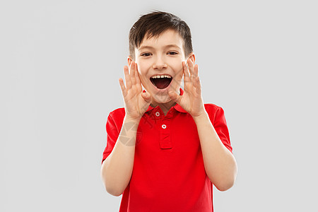 童,表情人的快乐的小男孩穿着红色马球T恤,灰色背景上大喊大叫打电话穿着红色马球T恤的男孩大喊大叫图片