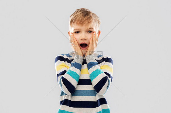 童,表情人的震惊的小男孩条纹套头衫,触摸他的脸灰色的背景震惊的小男孩穿条纹套衫图片