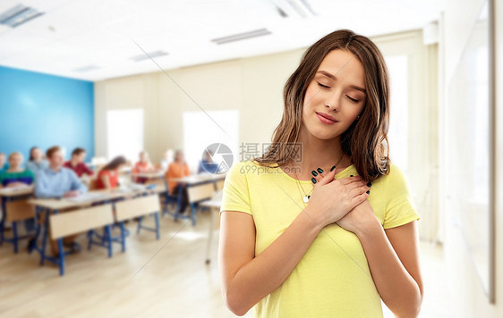 学校,教育真诚的情感感谢十几岁的学生女孩,闭着眼睛,穿着t恤,双手放胸前教室背景下的心脏上学生女孩学校图片