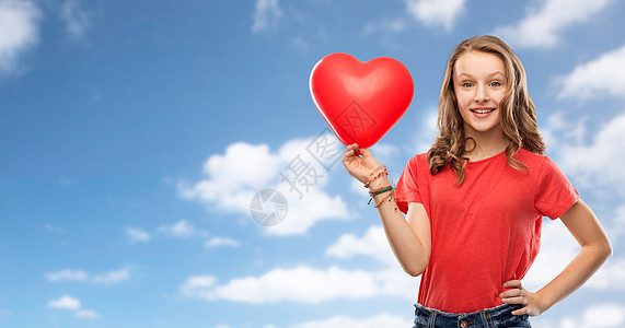 情人节,爱人的微笑美丽的十几岁女孩,留着长发,穿着红色T恤,蓝天云层背景上着心形气球带着红色心形气球的微笑少女图片