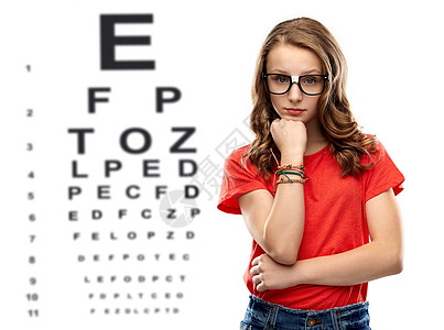 视觉,视力眼镜十几岁的学生女孩戴眼镜红色T恤思考眼睛测试图表背景戴眼镜的十几岁女孩超过了眼睛测试图图片