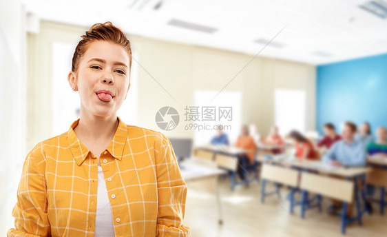 人们的微笑的红头发十几岁的学生女孩穿着格子衬衫,灰色的背景上展示她的舌头红头发的学生女孩学校表现出舌头图片