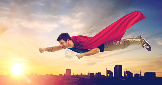 超级力量人的快乐的轻人红色超级英雄斗篷日落上空飞行塔林背景城市穿超级英雄斗篷的人城市日落上空飞行图片