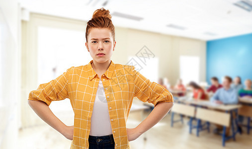 人们的高兴的红头发十几岁的学生女孩穿着格子衬衫,双手放臀部灰色背景学校里红头发的女学生很高兴图片