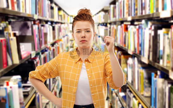 手势,计数人们的严肃的红头发十几岁的学生女孩穿着格子衬衫,手指指向图书馆的背景严肃的红头发学生女孩图书馆警告图片
