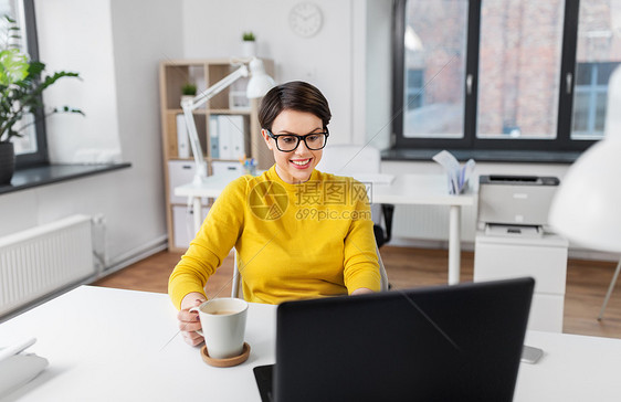 商务,休息人的微笑的女商人戴着眼镜,着笔记本电脑办公室喝咖啡女商人办公室着笔记本电脑喝咖啡图片