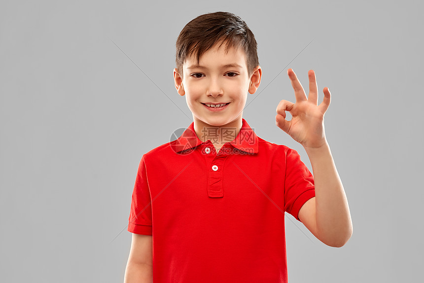 童,手势人的微笑的小男孩红色马球T恤OK手标志灰色背景微笑的男孩穿着红色的t恤,OK的手牌图片