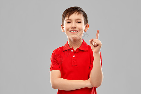 童,想法人的快乐的小男孩穿着红色马球T恤,手指指向灰色背景快乐的小男孩穿着红色的t恤,手指指向图片