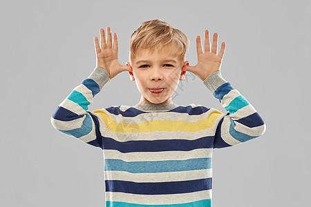 童,表情趣的快乐的小男孩穿着红色马球T恤,用手灰色背景上大耳朵穿红色T恤的小男孩用手大耳朵图片