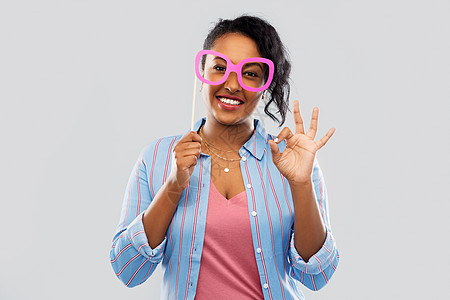 派道具,照片亭人的快乐的非裔美国轻妇女戴着大眼镜,灰色背景上OK手标志带着大眼镜的快乐非裔美国女人图片