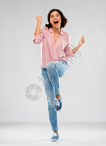 时尚,成功人们的快乐的微笑轻妇女穿着条纹衬衫,牛仔裤运动鞋庆祝胜利的灰色背景穿着衬衫牛仔裤的轻女人庆祝成功图片