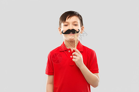 派道具,照片亭童的微笑的小男孩穿着红色马球T恤,黑色胡子灰色背景上带着黑色胡子的红色T恤微笑的男孩图片