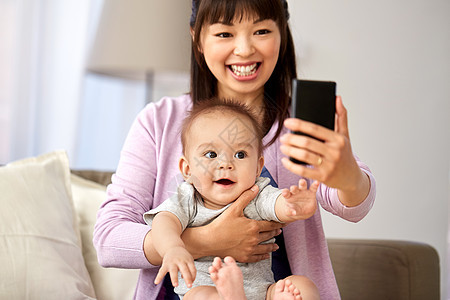 轻亚洲母亲与小婴儿用智能手机自拍图片