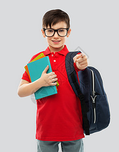 学校,教育人的微笑的小学生男孩穿着红色马球T恤,戴着眼镜,带着书灰色背景的袋子带着书包的眼镜微笑的小学生图片