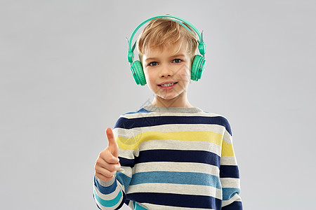 技术,音频设备人的微笑的小男孩耳机条纹套头衫听音乐拇指灰色背景戴耳机的男孩竖大拇指图片