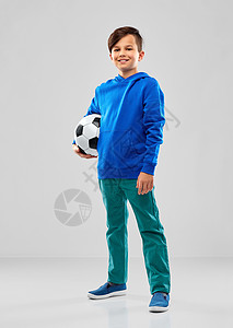 童,足球体育微笑的男孩蓝色帽衫与足球灰色背景穿着蓝色帽衫带足球的微笑男孩图片