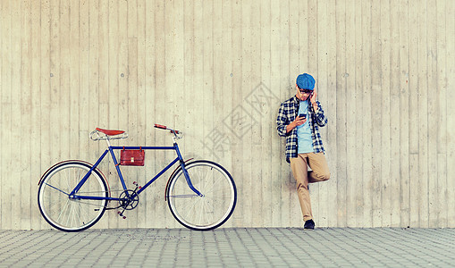 人,风格,技术,休闲生活方式轻的时髦男子戴着耳机,智能手机固定齿轮自行车城市街道墙上听音乐戴着智能手机自行车的耳背景图片
