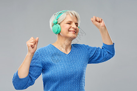 技术老人的微笑的老妇女戴着眼镜耳机,灰色背景下听音乐戴耳机听音乐的高级女人图片