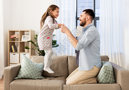 家庭,童父亲的快乐的父亲小女儿跳沙发上,家里玩得开心父亲女儿家里蹦蹦跳跳,玩得很开心图片