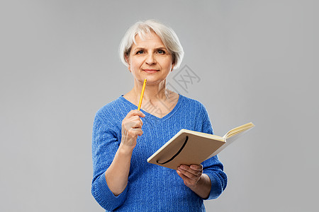 穿蓝色毛衣的老年女子拿着日记笔在思考图片