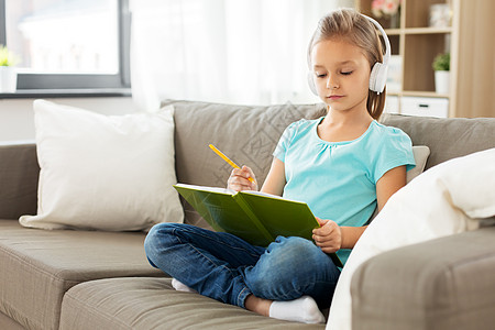 人,童睡觉时间的小女孩戴着耳机,着日记铅笔坐家里的沙发上女孩戴着耳机,家里沙发上写日记图片