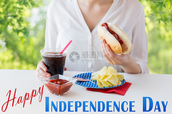 美国独立日,庆祝假日妇女抱着热狗可乐塑料杯与薯片番茄酱7月4日绿色自然背景特写女人用可口可乐吃热狗图片