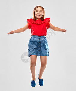 童,趣运动的快乐的微笑女孩穿着红色衬衫裙子跳过灰色的背景快乐的微笑女孩穿着红色衬衫裙子跳跃图片