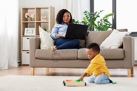 家庭母亲人的快乐的非裔美国母亲用笔记本电脑小儿子家里玩玩具积木套件妈妈用笔记本电脑婴儿玩玩具块图片