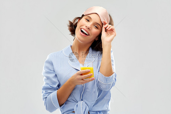 人们睡前的快乐的轻女人睡衣眼罩,着杯橙汁灰色的背景女人睡衣带果汁的睡觉具图片