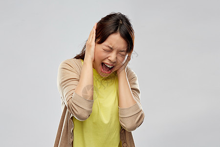 人,情感压力的亚洲轻女人用手闭着耳朵,灰色的背景下尖叫紧张的亚洲女人闭着耳朵尖叫图片