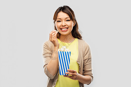 快餐人们的微笑的亚洲妇女吃爆米花条纹桶灰色背景微笑的亚洲女人吃爆米花图片