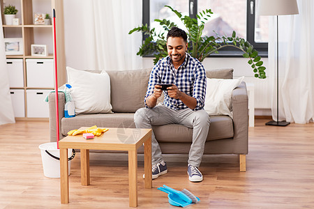 家庭技术印度男子清洁家庭后智能手机上玩游戏男人打扫家后智能手机上玩游戏图片