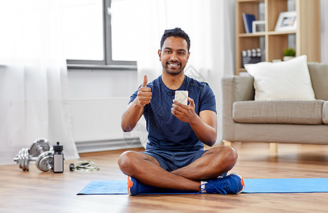 运动,技术健康的生活方式微笑的印度男人,智能手机坐运动垫上,家里竖大拇指印度男人家里用智能手机运动垫上图片