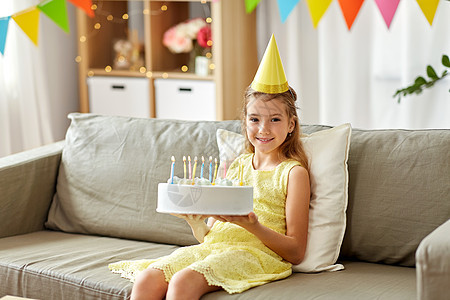 童庆祝快乐的女孩戴着派帽,家里生日蛋糕家里戴着生日蛋糕的派帽的好女孩图片