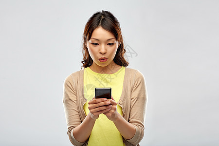 技术人的惊讶的亚洲妇女用智能手机灰色背景惊讶的亚洲女人用智能手机图片