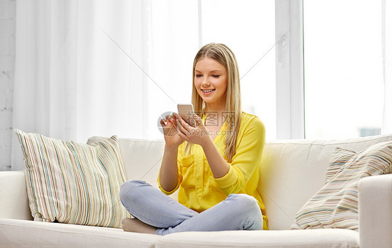 技术互联网微笑的轻妇女十几岁的女孩,智能手机坐家里的沙发上轻的女人十几岁的女孩家里智能手机图片