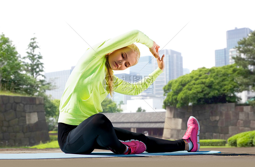 健身,运动健康的生活方式妇女伸展运动垫夏季公园东京城市背景城市公园的运动垫上伸展的女人图片