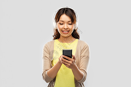 人,技术音频设备的快乐的亚洲轻妇女耳机听音乐智能手机灰色背景戴耳机听音乐的亚洲女人图片