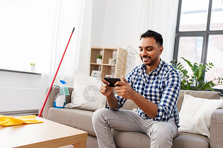 家庭技术微笑的印度男子智能手机上玩游戏后,打扫家男人打扫家后智能手机上玩游戏图片