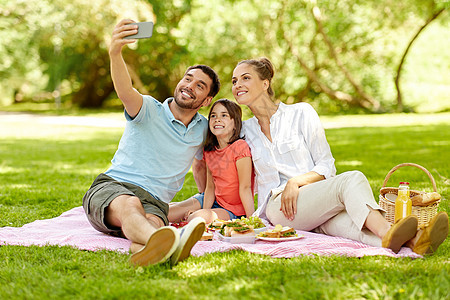 家庭,休闲技术快乐的母亲,父亲女儿野餐自拍智能手机夏季公园家人公园野餐自拍图片