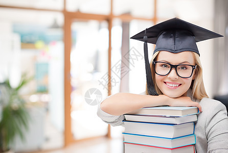 教育,毕业知识快乐的微笑研究生女孩戴着学士帽眼镜,带着学校背景的书籍研究生女孩戴着带书的学士帽图片
