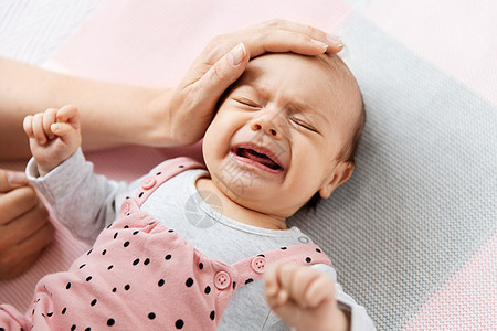 婴儿期,母亲人的母亲的手触摸哭泣的小婴儿女儿躺编的毯子上母亲的手抚摸着哭泣的小女儿图片