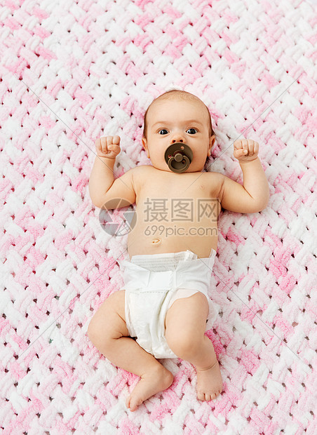 婴儿期人们的甜蜜的小女孩尿布上躺着,用奶嘴毛绒纱的针粉红色毯子上穿着尿布的女婴躺毯子上用奶嘴图片