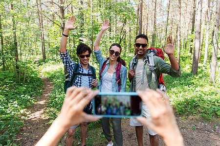 徒步旅行拍照旅行,旅游徒步旅行的群朋友,背包挥舞着手,森林里被智能手机拍照带背包的朋友徒步旅行中被拍照背景