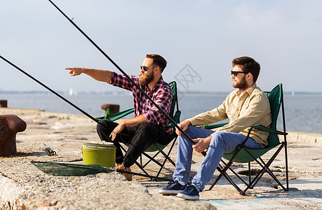 休闲人的男朋友与钓鱼竿坐营地椅子上的海上码头码头上钓竿的男朋友图片