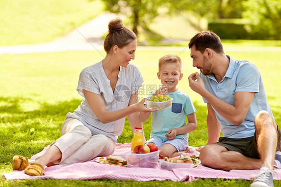 家庭,休闲人的快乐的母亲,父亲小儿子夏季公园野餐吃葡萄快乐的家庭夏天的公园野餐图片